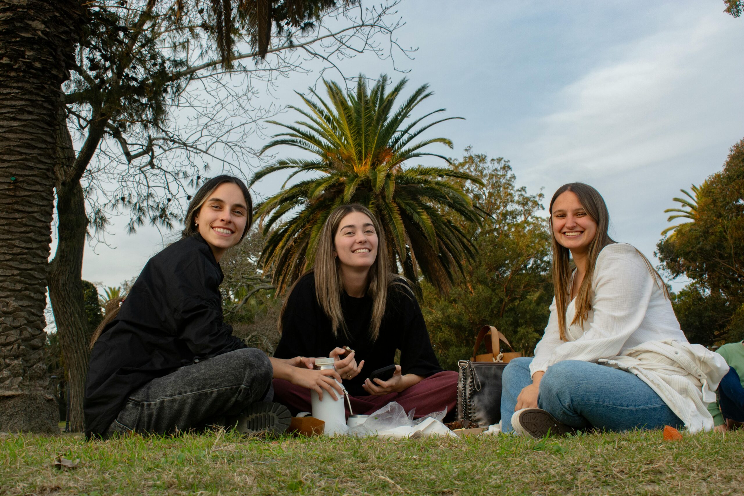 Three young adults enjoy a picnic outdoors, creating a joyful and relaxed atmosphere.